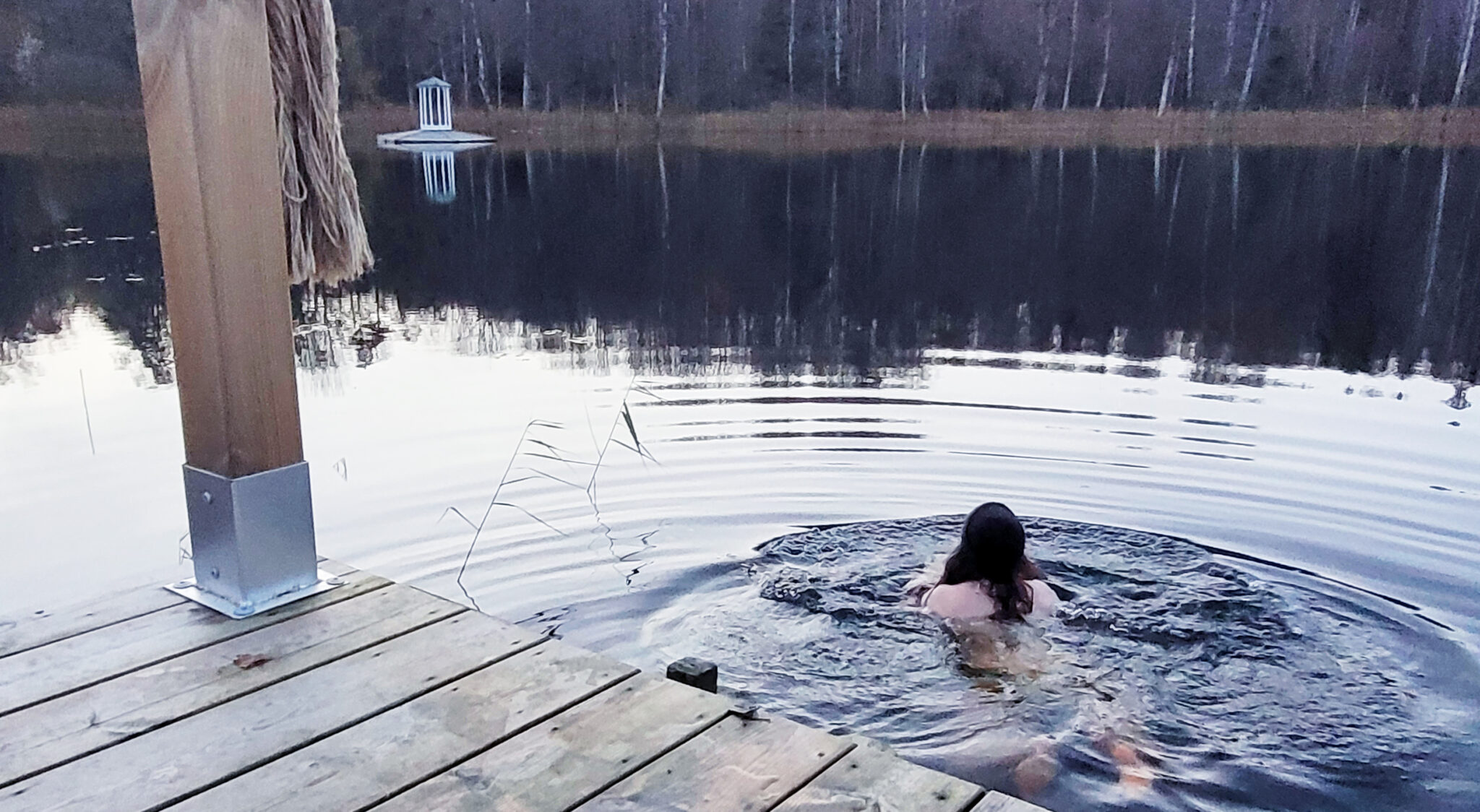 En tjej iklädd mössa simmar ut i det kalla mörttjärnet.